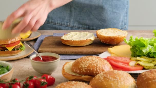 Baker nő hamburgert főz. A nő zsemléből, szeletekből, salátából, uborkából, paradicsomból, hagymából és szószból főz hamburgert. Gyönyörű háttér. Gyorsított mozgás. — Stock videók