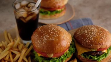 Fast food. Makro, hamburger, patates kızartması, kola. Bir kadın çörek, pirzola, marul, salatalık, domates, soğan ve sostan hamburger yaptı. Güzel arka plan. Yavaş çekim.