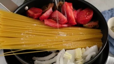 Kadın spagetti hazırlıyor. Tavaya tuz, baharat, fesleğen ve zeytinyağı ekler.