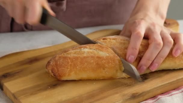 Mulher cortando pão baguete orgânico caseiro e cortando-o em pedaços na placa de corte. — Vídeo de Stock