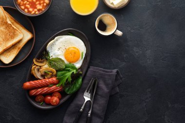 Geleneksel İngiliz kahvaltısı kızarmış yumurta, sosis, fasulye, mantar, siyah arka planda ızgara domates..