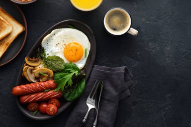 Geleneksel İngiliz kahvaltısı kızarmış yumurta, sosis, fasulye, mantar, siyah arka planda ızgara domates..