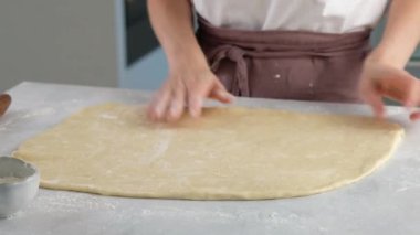 Hamuru merdaneyle yuvarlayıp hamuru şekillendiriyor. Masada un içinde hamur yoğuran kadın eller. Kapatın. Tarçınlı çörek üretimi. Fırın ürünleri.