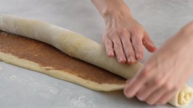 Pasta şefi çörek için tarçınlı hamur rulosu sarar. Kadın elleri masada tarçınlı kek hazırlıyor. Kapatın. Tarçınlı çörek üretimi. Fırın ürünleri. Aperatif tarçınlı çörekler