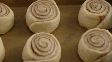 Pasta şefi çörek için tarçınlı hamur rulosu sarar. Kadın elleri masada tarçınlı kek hazırlıyor. Kapatın. Tarçınlı çörek üretimi. Fırın ürünleri. Aperatif tarçınlı çörekler