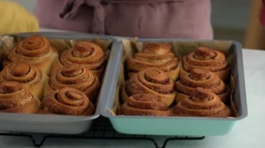 Kadın fırından tarçınlı rulo çıkardı. Tarçınlı ruloların üzerine tatlı krem peynir kreması dökülüyor. Tarçınlı rulo üretiliyor. Fırın ürünleri. Aperatif tarçınlı çörekler