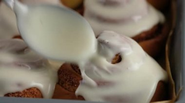 Taze pişmiş tarçınlı çöreklere ya da Cinnabon 'a krema dök. Tarçınlı ruloların üzerine tatlı krem peynirli krema dökülüyor. Tarçınlı çörek üretimi. Fırın ürünleri. Aperatif tarçınlı çörekler