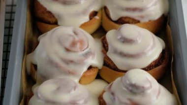 Taze pişmiş tarçınlı çöreklere ya da Cinnabon 'a krema dök. Tarçınlı ruloların üzerine tatlı krem peynirli krema dökülüyor. Tarçınlı çörek üretimi. Fırın ürünleri. Aperatif tarçınlı çörekler