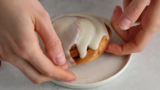 Ženské ruce lámou skořicovou housku na talíři. Čerstvě upečené skořicové rolky nebo Cinnabon zblízka. Sladký smetanový sýr na skořicových rolích. Výroba skořicových rohlíků. Předkrm skořicové buchty — Stock video