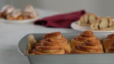 Tarçınlı rulo ekmeği bir tabakta yakın plan kesim. Tarçınlı ruloların üzerine tatlı krem peynirli krema dökülüyor. Tarçınlı çörek üretimi. Fırın ürünleri. Aperatif tarçınlı çörekler