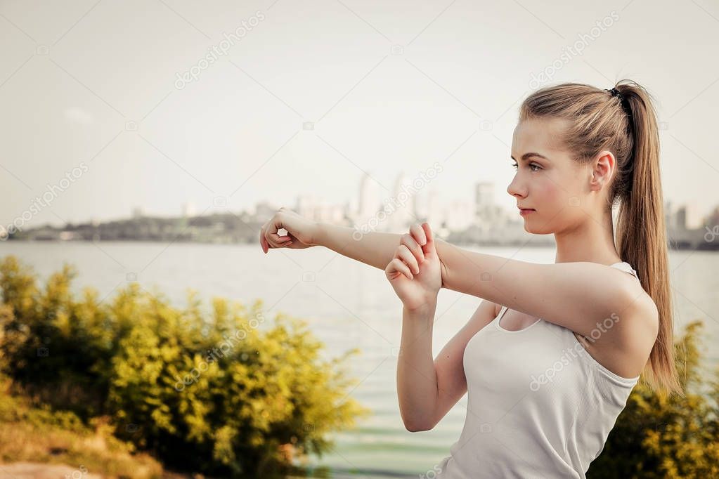 The girl make stretching exercise. Young woman standing on the city background and looking sideways