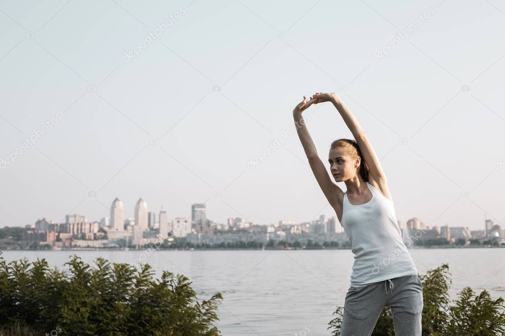 Young and slim woman doing sport exercise on city background. Pretty girl stretching and warm up.