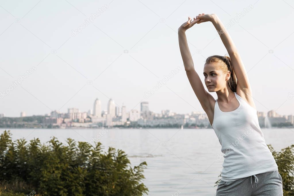 Young woman stretching outdoor. The Pretty girl with blond hair doing exercise on city background.