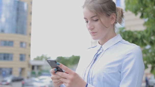 年轻的女商人用她的移动智能手机上网冲浪 站在街上的女孩在城市背景上 — 图库视频影像