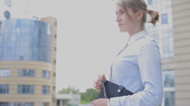 自信的妇女在上衣与笔记本和钢笔站在建筑物背景上 — 图库视频影像