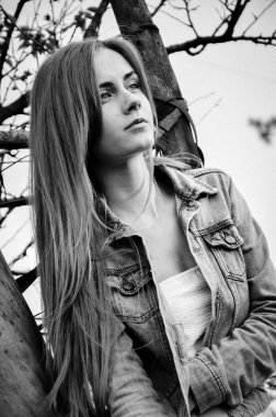 Kendine güvenen kız ağaca yaslanmış düşünceli bakışla siyah beyaz portre. Şık giysiler içinde genç ve güzel kadın portresi. Model kameraya poz. Bir yaşam tarzı. Moda