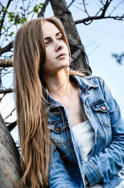 Kendine güvenen kız ağaca yaslanmış düşünceli bakışla. Şık giysiler içinde genç ve güzel kadın portresi. Model kameraya poz. Bir yaşam tarzı. Moda