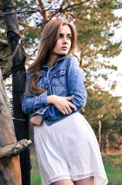Güzel model duran ve üzerinde ahşap eskrim eğilerek sarı saçları ile. Ellerini karnına çarpı işareti vardır. Sol tarafta onu kollamaya modeli. Açık. Kırsal.