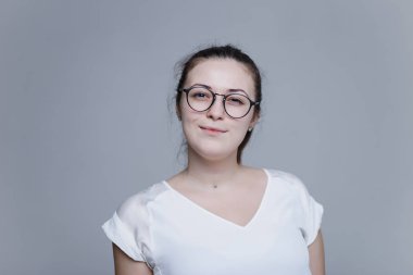 Şirin Avrupa kadın kameraya bakıyor. Gözlük takan ve beyaz bluz ve kolye giymiş kız. Zeki görünüyor 
