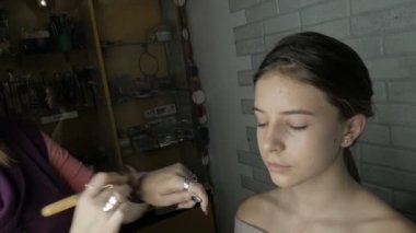Makyöz makyaj genç bir kıza yapar. Sanatçı modeli yüzünde cilt tonunu dengeler. Fırça ile çalışır. Kozmetik. Yüz tedavi. Cilt Bakımı. 