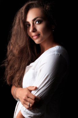 Sevimli ve güzel genç kadın düşük anahtar ışık kamera poz. Karamel tenli kadın modeli. Uzun kıvırcık dalgalı kahverengi saçlı Genç ve güzel kadın portresi