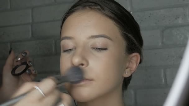 艺术家甚至出模型肤色与刷子 化妆师给一个年轻女孩化妆 艺术家在模特脸上变亮肤色 使用画笔 化妆品 面部护理 皮肤护理 — 图库视频影像
