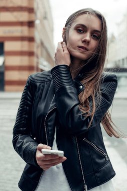 Şehirde akıllı telefon kullanan bir kadın. Deri ceketli, uzun saçlı güzel bir kadın. 