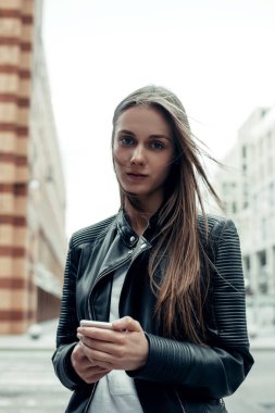 Şehirde akıllı telefon kullanan bir kadın. Deri ceketli, uzun saçlı güzel bir kadın. 