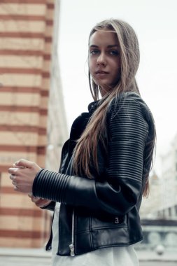 Şehirde akıllı telefon kullanan bir kadın. Deri ceketli, uzun saçlı güzel bir kadın. 