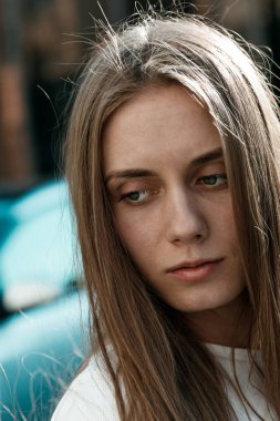 Sarı saçlı ve mavi gözlü genç bir kadının dikey portresi. Sokakta kameraya poz veren model