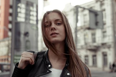 Omzunda sırt çantasıyla, başını kaldırmış kameraya bakan modaya uygun genç bir kadın. Gururlu ve kendinden emin genç bir kadın.