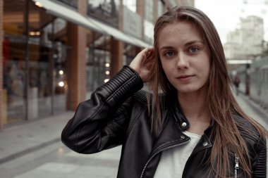 Güzel sarışın kadın kameraya bakıyor ve saçına dokunuyor. Deri ceketli kız.