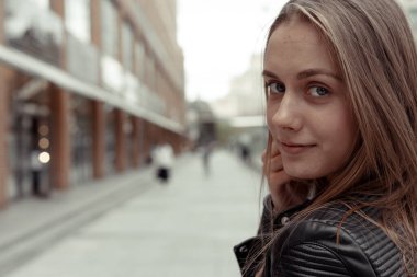 Güzel sarışın kadın kameraya bakıyor ve gülümsüyor. Deri ceketli kız.