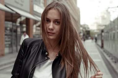 Uzun sarı saçlı geniş açılı portre kadın. Kadın model kameraya bakıyor ve saçlarıyla oynuyor. Siyah eko-deri ceket giyen şık bir genç kadın.