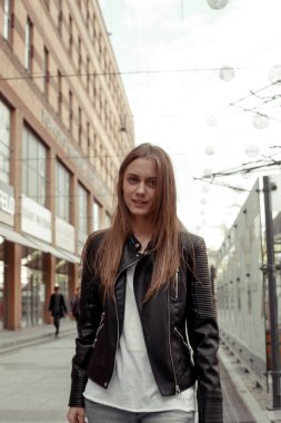Kameraya bakan kendine güvenen genç bir kadın. Siyah eko deri ceket giyen sarı saçlı güzel bir kız. Model yürüyüşü 