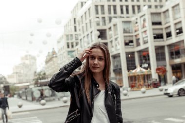 Sarışın, genç bir kadın kamerada poz veriyor. Siyah deri ceket giyen kız. Kadın saçına dokunuyor.