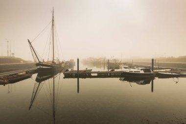 Balıkçı tekneleri bekleyen kalkış Bruinisse, Zeeland, Harbour gündoğumu sırasında yoğun sis nedeniyle ertelendi. Sakin su ve tekneler ve liman ile bir peacefull sahne.