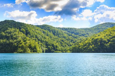 Dağlar ile yeşil ağaçlar ve mavi gökyüzü ve su ile yaz güneşli manzara. Plitvice Gölleri, Hırvatistan