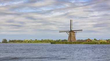Bulutlu gökyüzü, yatay ve Rotterdam yakınındaki Rottemeren gölde bulunan eski Hollanda geleneksel yel değirmeni.