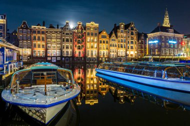 Amsterdam Damrak geleneksel Hollanda mimarisi geceleri. Ön planda tur tekneleri.