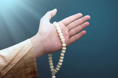 Müslüman erkek parlak arka plan üzerinde tespih tutan