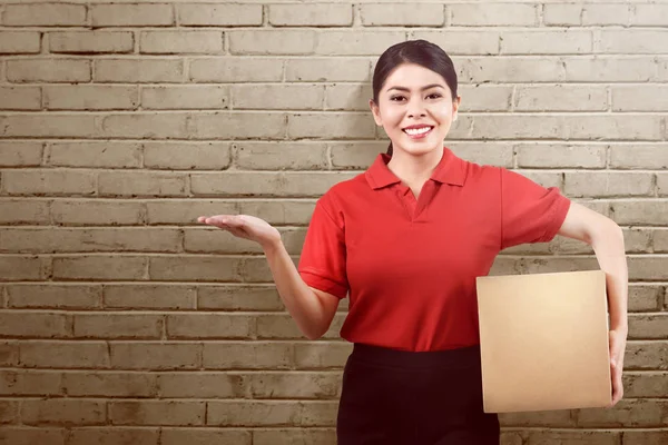 Asiática Entrega Mujer Holding Paquete Mostrando Algo Sobre Ladrillo Pared —  Fotos de Stock