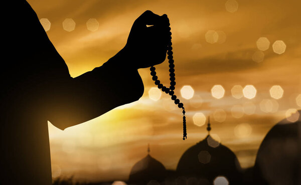 Silhouette of muslim man praying with prayer beads during sunset 