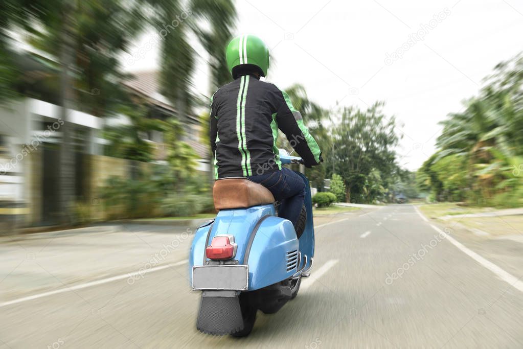 Back view of motorcycle taxi driver with blue scooter on urban street