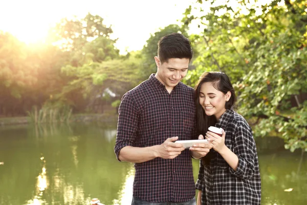 湖背景を備えた公園のタブレットで魅力的なアジア カップル — ストック写真