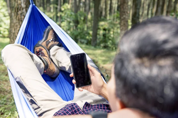 男子使用他的手机 而放松在吊床上的森林 — 图库照片