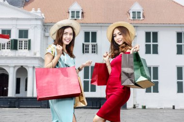 Şehrin üzerinde birçok alışveriş torbaları elinde şapka ile genç iki Asyalı kadın