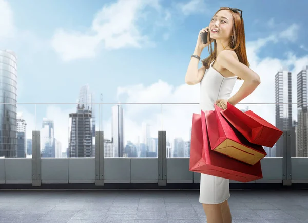 魅力的なアジアの女性のモールのバルコニーで買い物袋を運んでいる間携帯電話を使用して — ストック写真