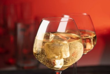 Parlak arka plan üzerinde beyaz şarap ve buz küpleri ile şarap kadehi çifti