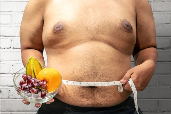 Fat man diet with fruit using measuring tape to measuring his stomach at home. Fat man diet